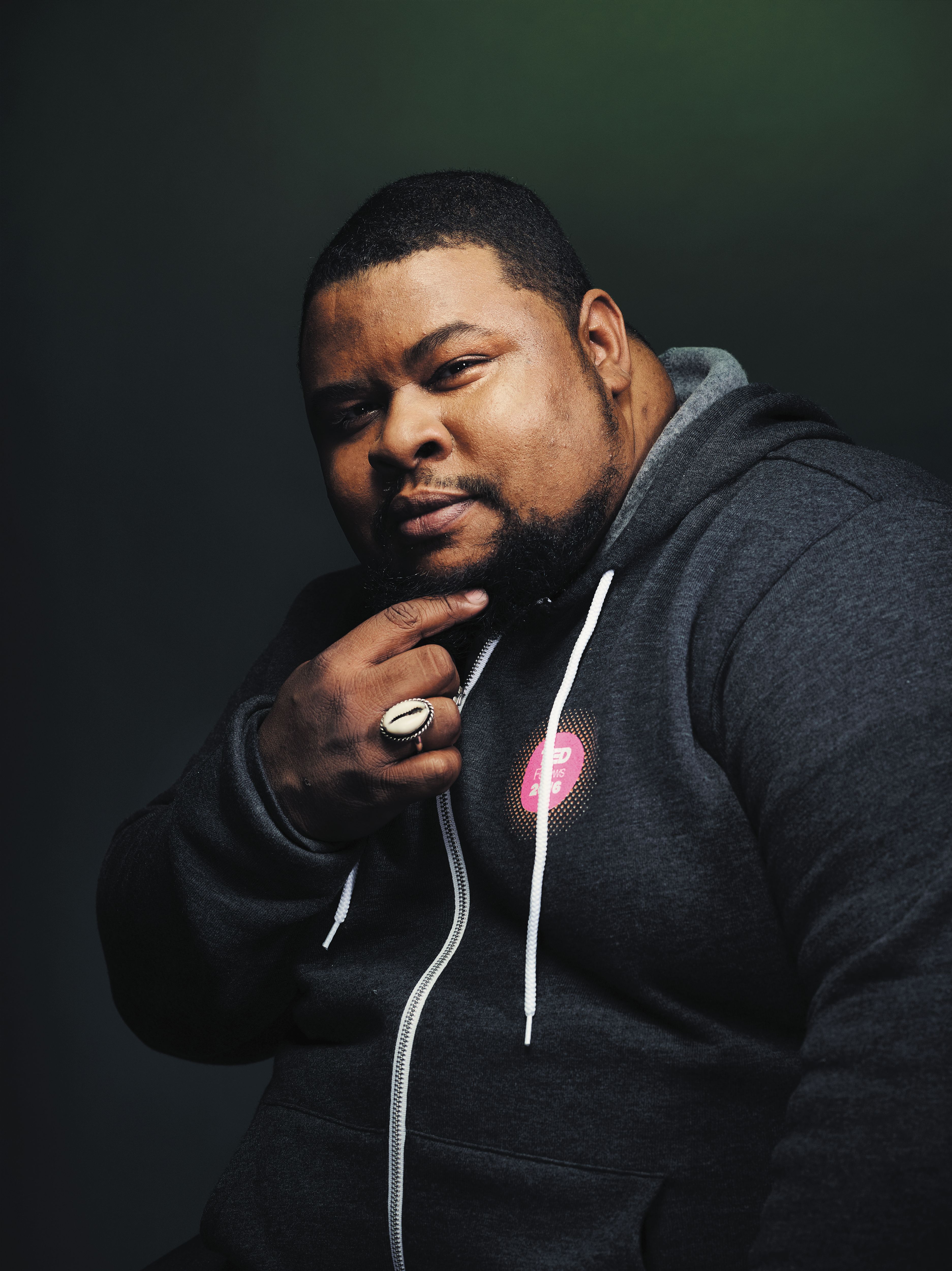 Portrait of Michael W. Twitty, wearing a zip-up hoodie and touching his beard.